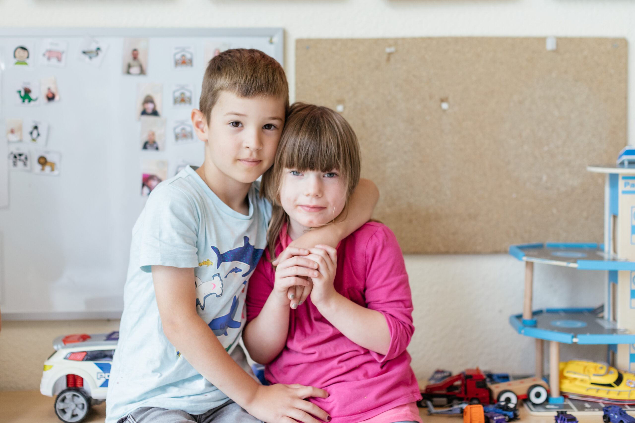 In einem Raum ist ein kleiner Junge mit einem kleinen Mädchen vor der Kamera. Der Junge umarmt das Mädchen.