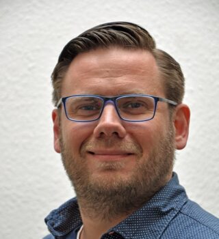 Ein GPS Mitarbeiter namens Mathias Knaack. Er trägt eine blaue Brille und einen Bart.