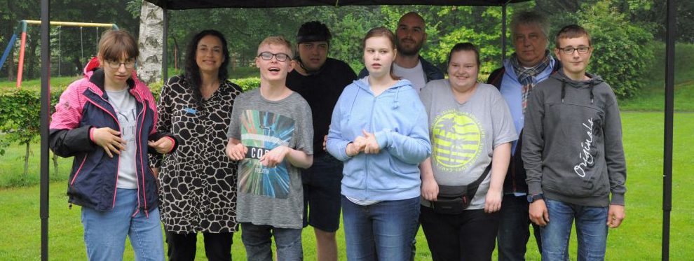 Man sieht Schüler und Lehrkräfte von der Schule draußen auf der Wiese unter einer Bedachung