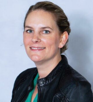 Janna Rohlfs: Eine lächelnde Frau mit mittellangen mittelblonden Haaren mit Zopf. Sie trägt Ohrringe.