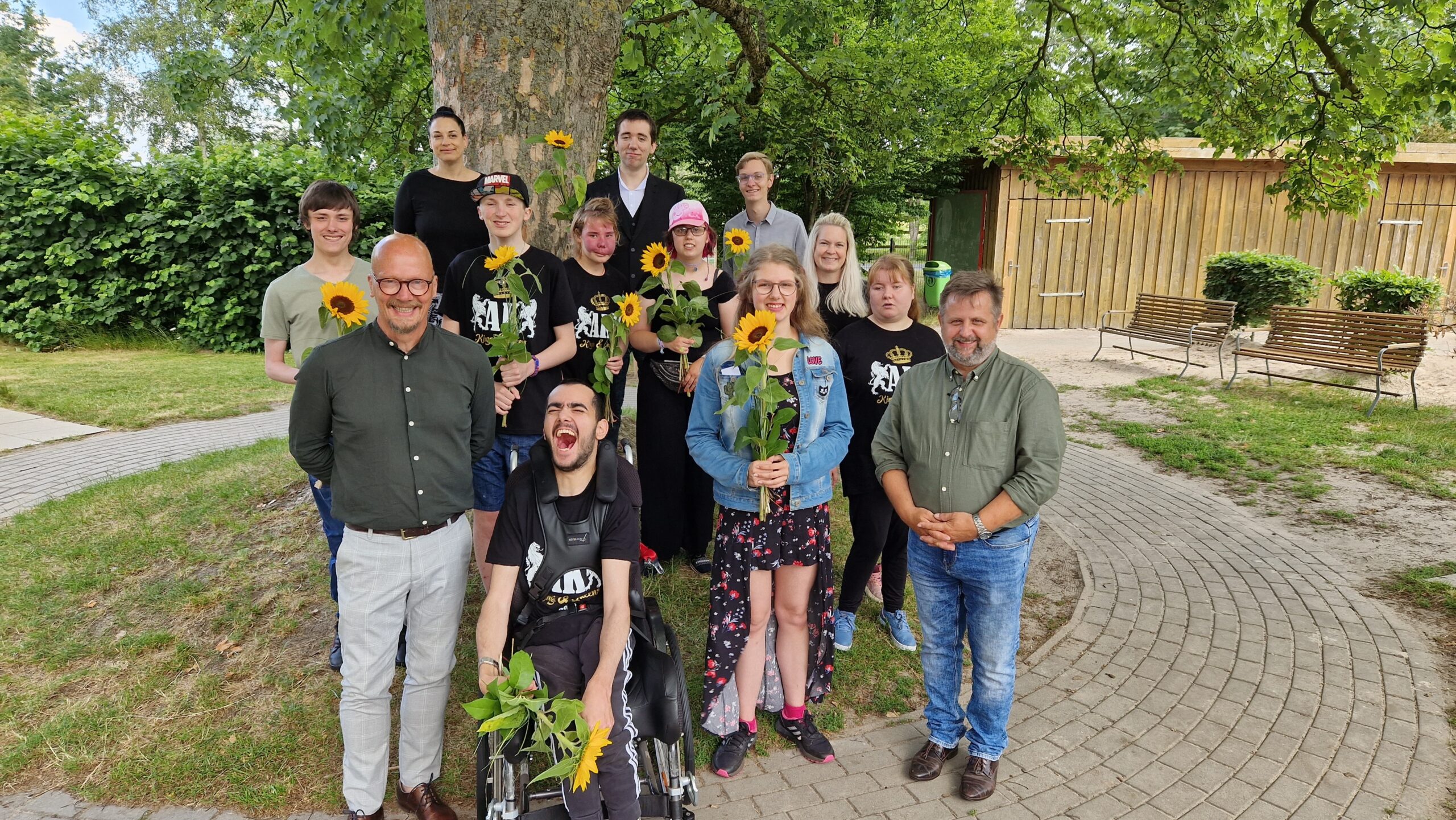 Man sieht junge Schüler von der Dorfschule Mansie und den Schulleiter Friedrich Fittje mit den Lehrern draußen im Garten bei Ihrer Verabschiedung. Die Schüler halten eine Sonnenblume in der Hand.