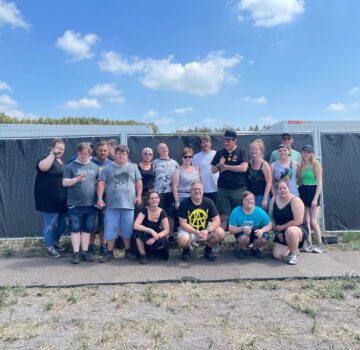 Eine Gruppe junger Menschen mit einer Behinderung stehen draußen vor einer Wand mit einer Betreuerin und den Fernsehstar Elton.