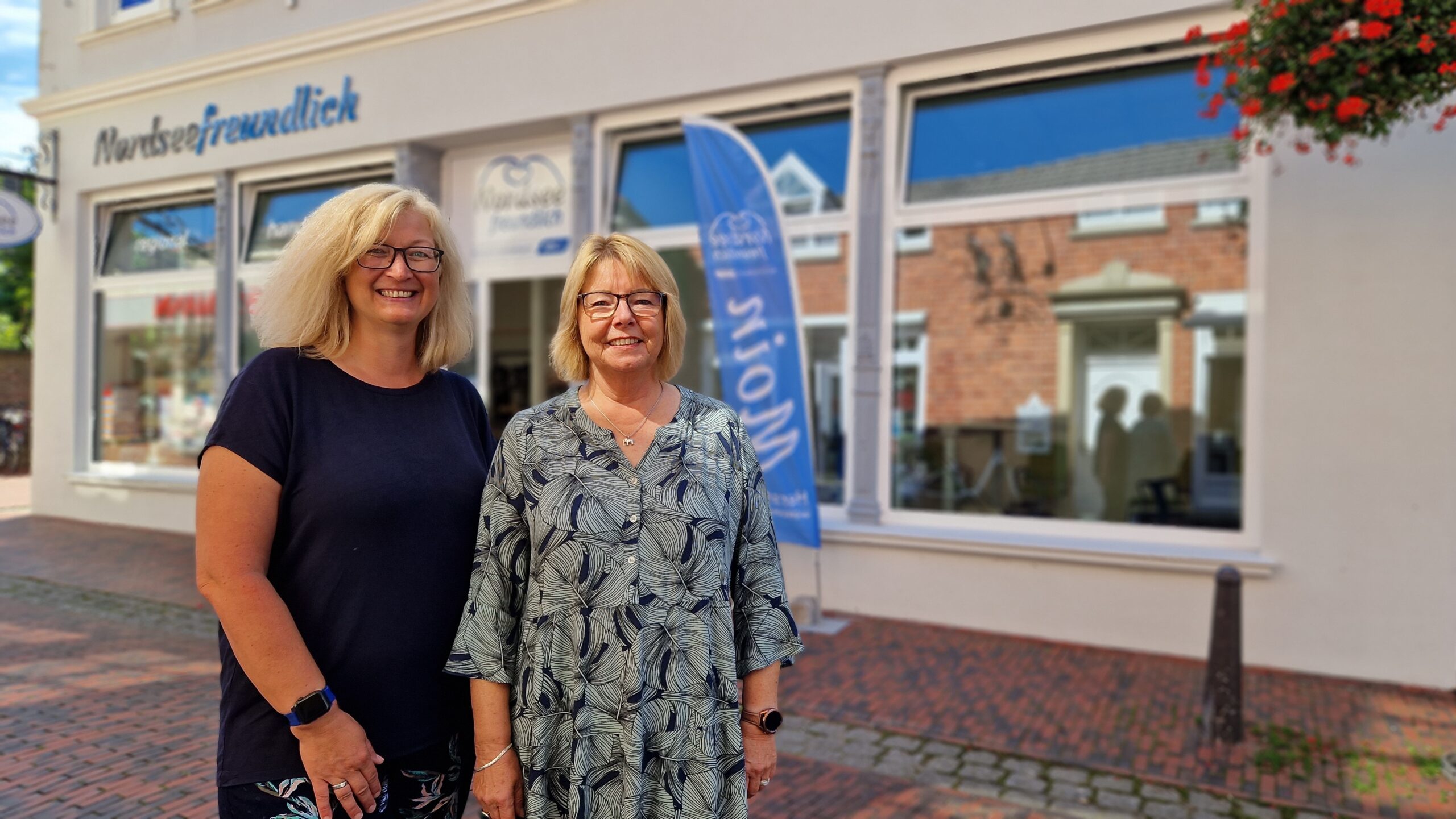Draußen vor dem GPS Laden "Nordseefreundlich" sieht man zwei GPS Mitarbeiterinnen namens Bianca Rieken und Petra Mingo stehen und schauen in die Kamera.