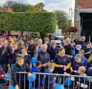 Man sieht draußen Erwachsene, Kinder und Jugendliche bei einem Fest. Im Hintergrund sieht man auch eine Bühne.
