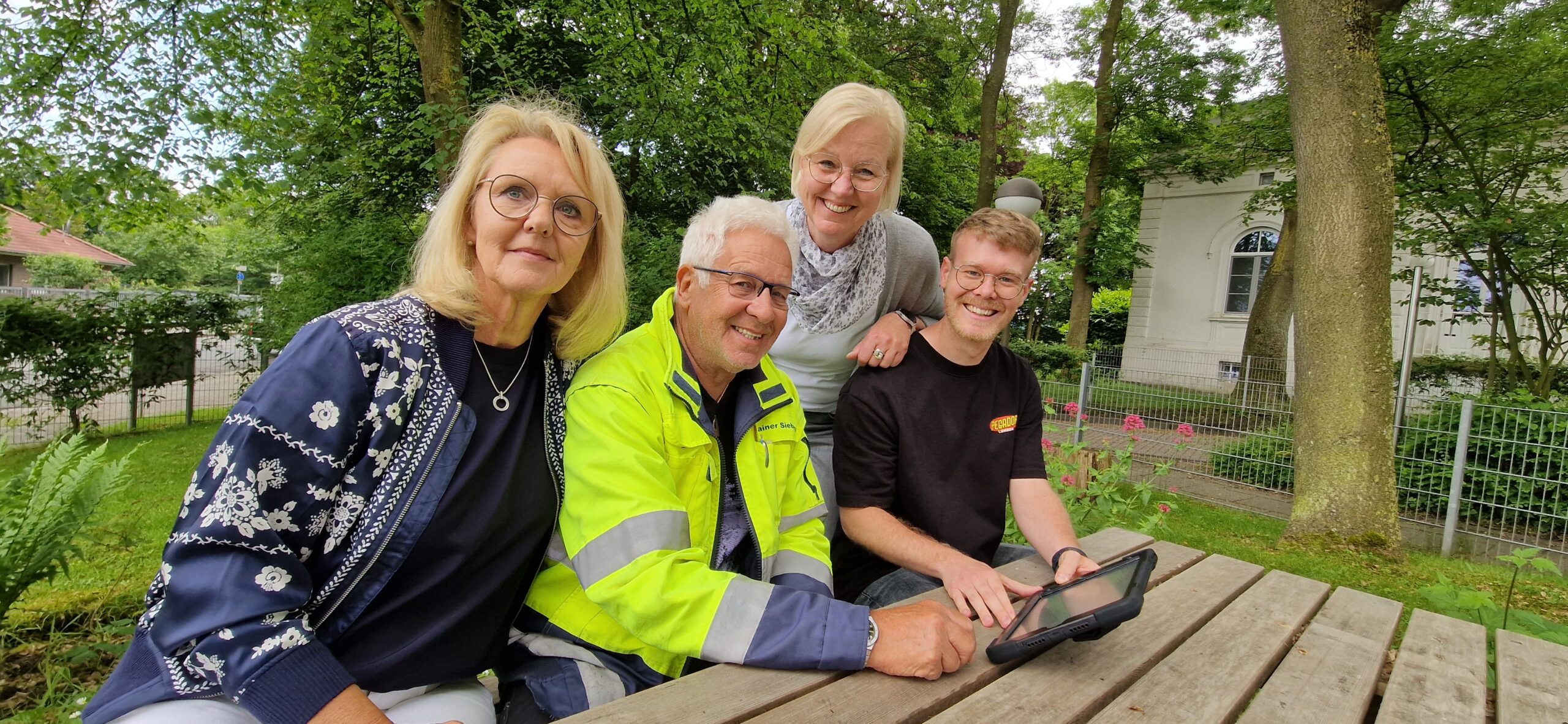 Zwei GPS Mitarbeiterinnen mit zwei Männern draußen im Garten am Tisch. Die zwei GPS Mitarbeiterinnen sind Sylvia Erhhardt Leiterin des "GPS Kindergarten Leuchtfeuer" und Britta Reusch-Sieberns von der "GPS Praxis für Logopädie".