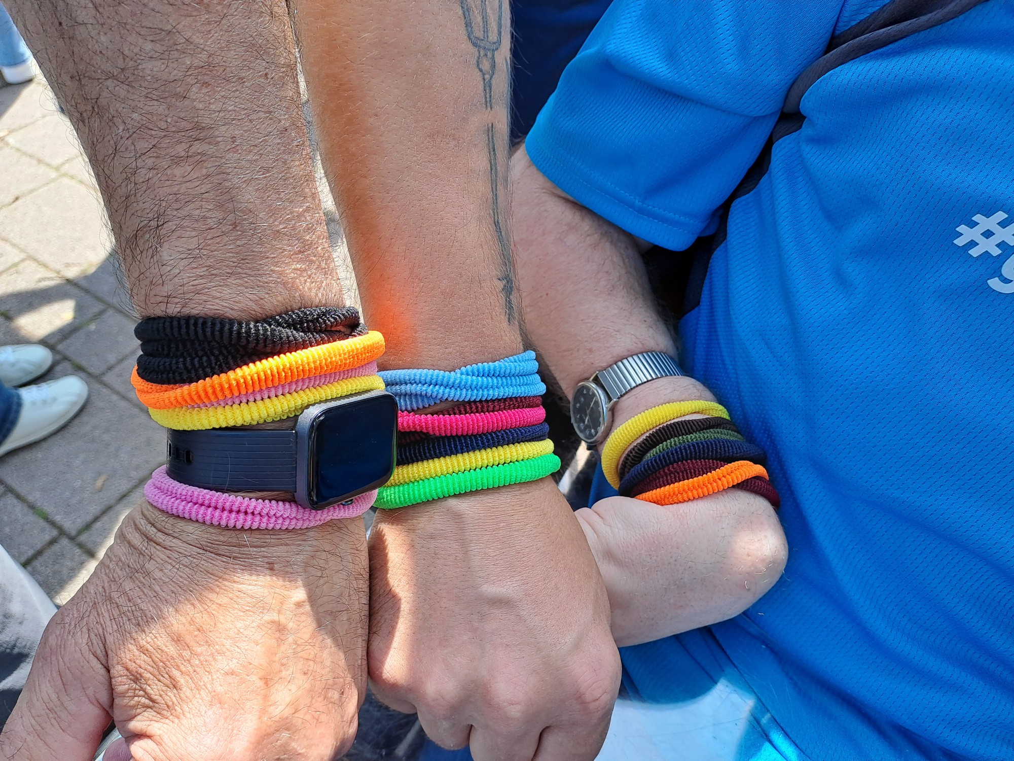 Drei Menschen zeigen ihre Arme mit verschiedenen bunten Armbändern.