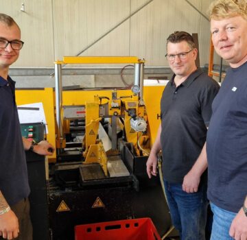 Gruppenfoto mit zwei Männern und einen jungen Mann vor einer Maschine in einer Werkstatt.