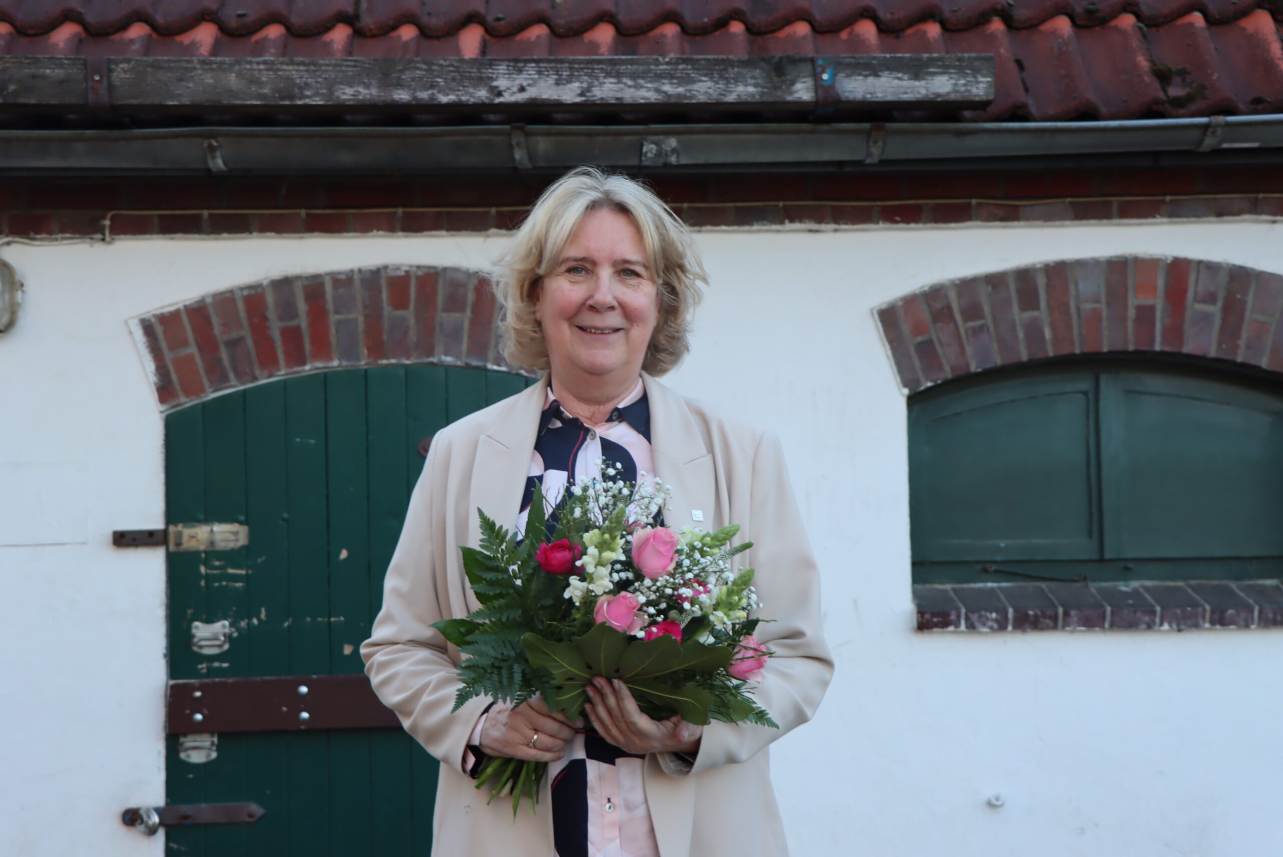 Verabschiedung der GPS Mitarbeiterin Sabine Gastmann. Sie hält draußen vor einem Gebäude einen Blumenstrauß. Sie war die Leiterin vom Heilpädagogischen Wohnverbund von der GPS.