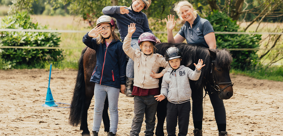 Eine Gruppe von jungen Kindern mit einer Trainerin beim Pferde reiten.