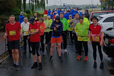Ein Gruppenfoto mit vielen Menschen vor der Kamera. Sie haben alle Sportsachen an. Draußen regnet es.