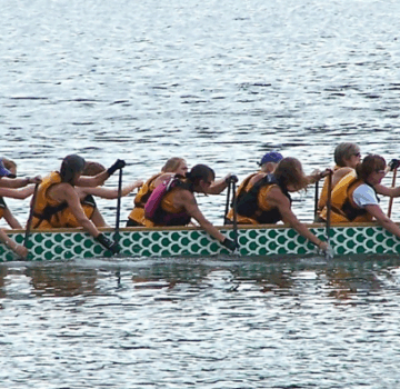 Viele Menschen rudern mit einem großen Drachenboot auf dem See.