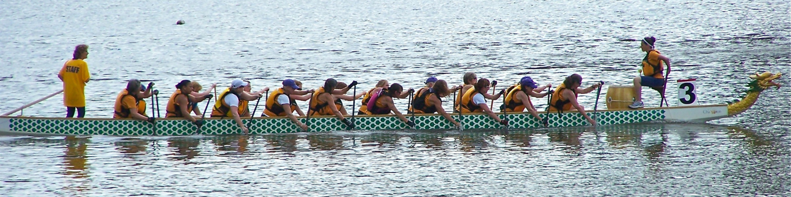 Viele Menschen rudern mit einem großen Drachenboot auf dem See.