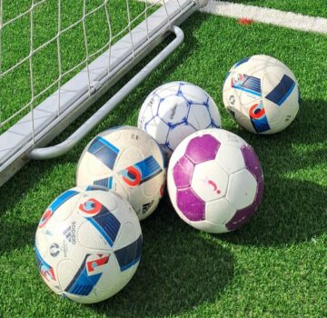 Fünf farbige Fußbälle neben ein Fußballtor
