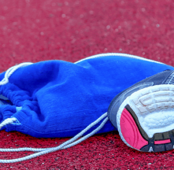 Zwei buntfarbige Sportschuhe, eine Trinkflasche und ein Turnbeutel auf einer Laufstrecke.