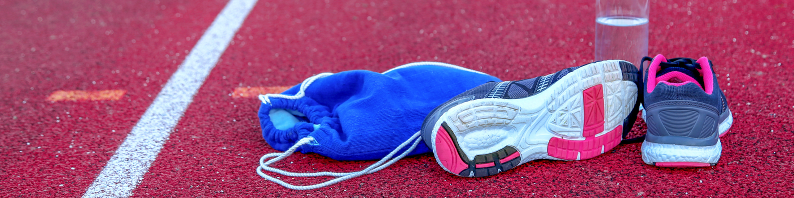 Zwei buntfarbige Sportschuhe, eine Trinkflasche und ein Turnbeutel auf einer Laufstrecke.