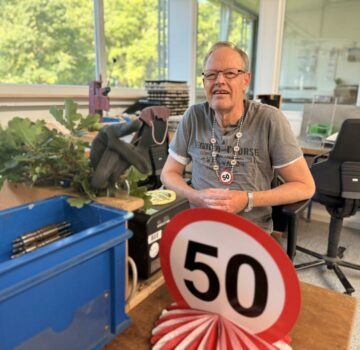 Ein GPS Beschäftigter feiert in der Werkstatt Jeringhave sein 50-jähriges Jubiläum. Er sitzt an seinem Arbeitsplatz. Man sieht ein rot-weißes Schild mit der Zahl "50".