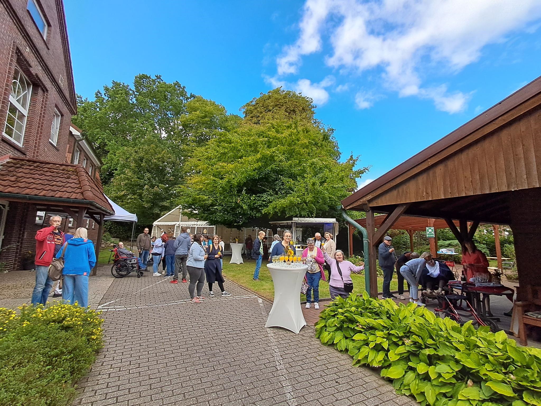Draußen bei schönen Wetter auf einem Innenhof bei einer Veranstaltung. Man sieht viele Menschen auf dem Bild.