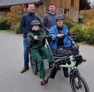 Ein Gruppenfoto mit einem GPS Mitarbeiter und drei junge Männer. Zwei Männer sitzen auf einen Lastfahrrad. Zwei Männer stehen dahinter. Im Hintergrund sieht man ein Haus.