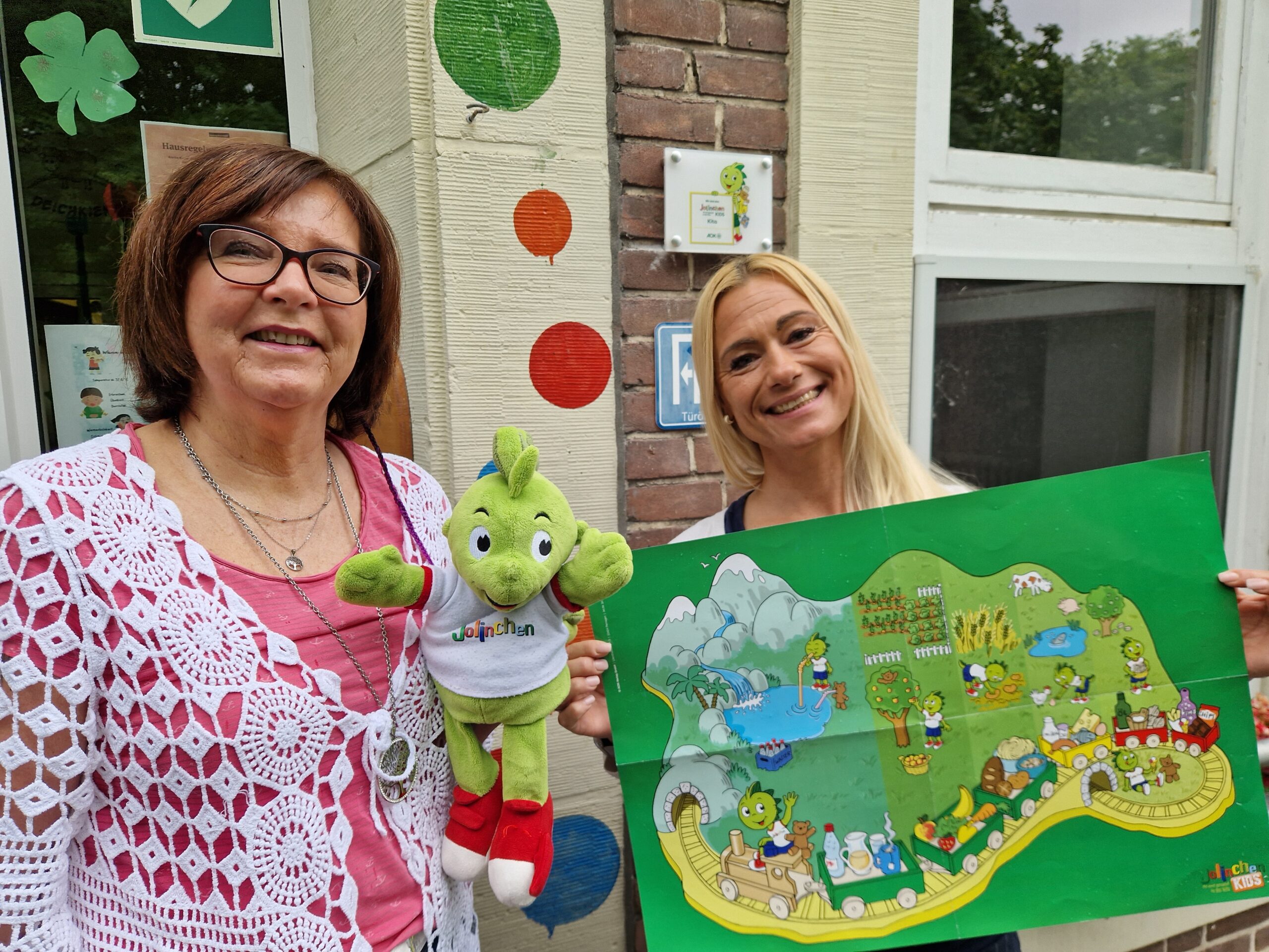 Zwei GPS Mitarbeiterinnen präsentieren eine Stoffpuppe und ein Kinderspiel aus Papier.