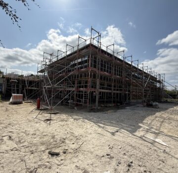 Draußen auf einer Baustelle sieht man ein großen Gebäude. Die Sonne scheint draußen.
