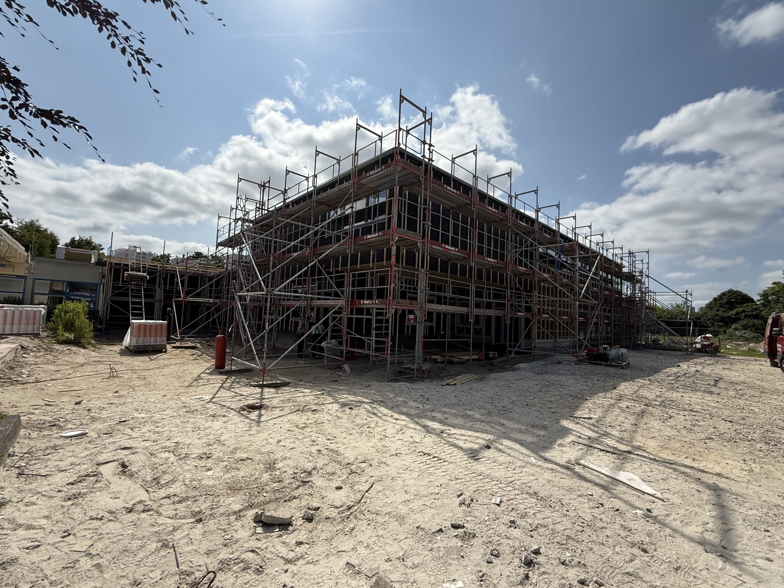 Draußen auf einer Baustelle sieht man ein großen Gebäude. Die Sonne scheint draußen.