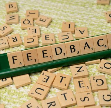 Auf dem Bild sieht man ein grünes Schild und Holzschilder mit verschiedenen Buchstaben. Aus den Buchstaben liest man das Wort "Feedback"
