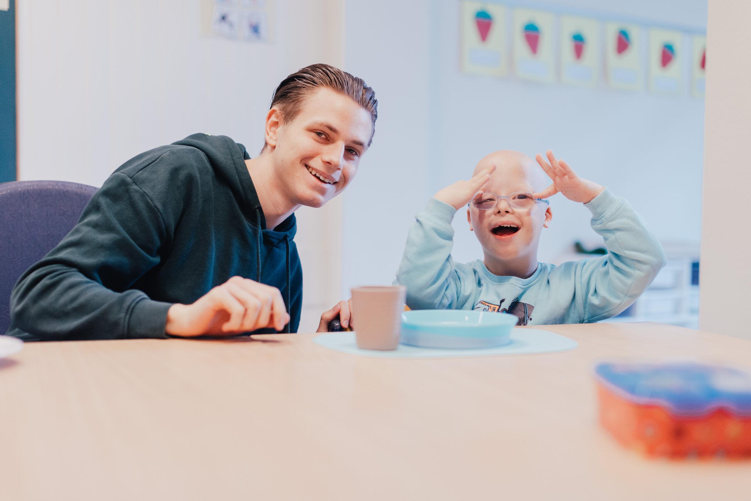 Ein junger Mann und ein kleiner Junge mit einer Behinderung sitzen an einem Tisch in einem Raum.