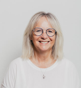 Eine Frau namens Kornelia Gebbert mit grauen schulterlangen Haaren und eine Brille. Sie trägt einen weißen Pullover.